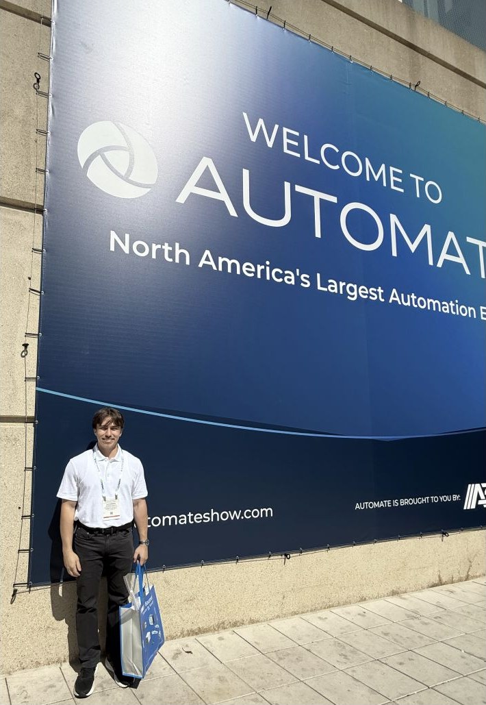 Alex standing in front of the Automate trade show welcome banner